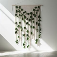 a white wall hanging with green plants on it's side in an empty room