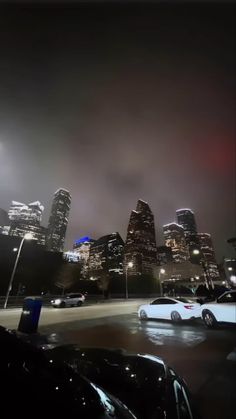 cars parked in a parking lot at night with city lights shining on the buildings behind them