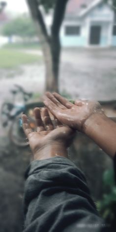 a person holding their hands out in front of a window with the rain coming down