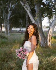 a woman in a white dress holding a bouquet of flowers and posing for the camera