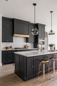 a large kitchen with black cabinets and white counter tops, gold bar stools and pendant lights hanging from the ceiling