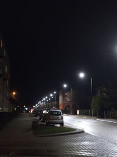 cars parked on the side of a street at night with bright lights shining in the background