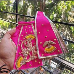 a hand is holding two pieces of pink cloth with gold embroidered designs on the sides