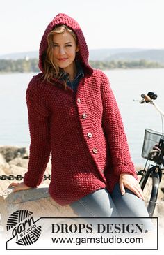 a woman in a red jacket sitting on a rock next to a bike and water