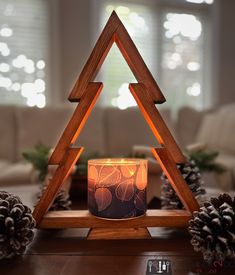 a lit candle sitting in front of a wooden triangle shaped stand with pine cones around it