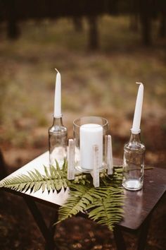 a table topped with candles and bottles filled with greenery on top of a forest floor