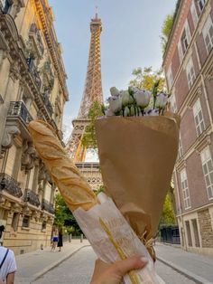 a person holding a baguette with flowers in front of the eiffel tower