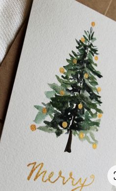 a card with a watercolor christmas tree on it and the words merry written in gold