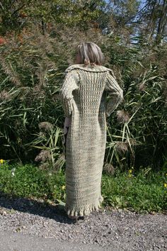 a woman in a long knitted dress standing on the side of a road with her back to the camera