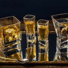 four glasses filled with liquid sitting on top of a wooden table next to other glassware