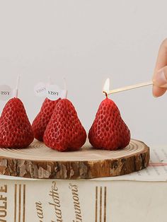 four strawberries on a wooden stand with a lit match between them