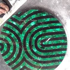 a manhole cover with green and black designs on the ground next to a sidewalk