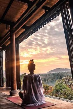 a woman sitting on top of a yoga mat in front of a window looking out at the mountains