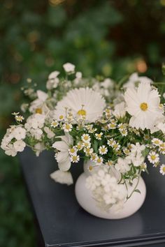 a white vase filled with lots of white flowers on top of a black table outside