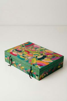 a green box with flowers painted on it sitting on a white surface, next to a black cord