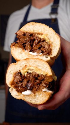 two halves of a sandwich with meat and sour cream on it, being held by a man in an apron