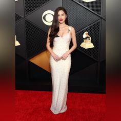 a woman in a white gown standing on a red carpet with an award behind her