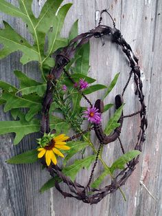 a wreath made out of barbed wire with flowers and leaves around it on the side of a wooden fence