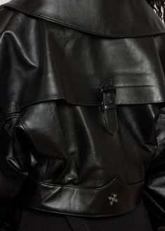 This oversized black leather jacket features a bold, structured design with voluminous sleeves and a wide collar. The jacket is accented by a diagonal front zipper and a wide belt that cinches the waist, blending avant-garde style with a sleek, modern edge. DETAILS: - Belted waist - Buckle embellishment on back - Option for stand collar COLOR: Black SIZE & FIT: Model is 32 bust, 25 waist, 38 hip and wearing a size S. CARE INSTRUCTIONS: Dry clean recommended. Air dry. Do not machine dry. Designer Black Outerwear With Belted Cuffs, Black Designer Outerwear With Belted Cuffs, Black Leather Outerwear With Belted Cuffs, Designer Oversized Black Outerwear, Designer Black Oversized Outerwear, Black Designer Oversized Outerwear, Chic Black Biker Jacket With Belt Loops, Designer Leather Outerwear With Belted Cuffs, Modern Black Outerwear With Belted Cuffs