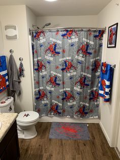 a bathroom with spiderman shower curtain, toilet and rugs on the wood floor