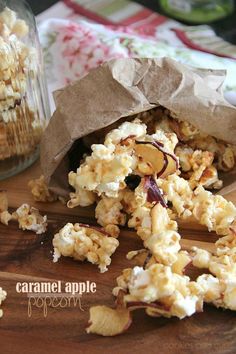 caramel apple popcorn on a wooden cutting board next to a jar of peanuts and a paper bag