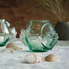 two green glass candle holders sitting on top of a white towel next to sea shells