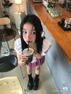 a girl with headphones on drinking from a cup while standing in front of a bar