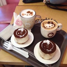 two desserts with hello kitty designs on them sit on a tray next to coffee cups