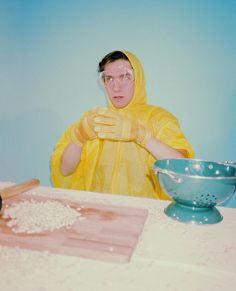 a man in a yellow raincoat and rubber gloves standing at a table with a blue bowl