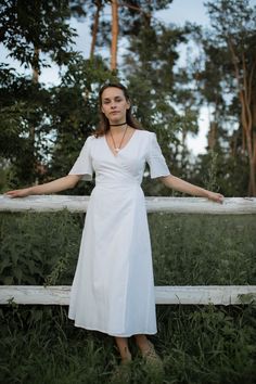 a woman in a white dress leaning on a fence