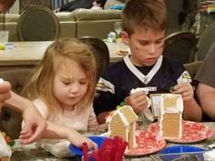 two children and an adult sitting at a table with gingerbread houses on plates in front of them