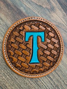 a leather patch with the letter t in it on a wooden surface and blue stitching