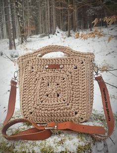 a crocheted bag sitting on top of a rock in the snow with a brown strap