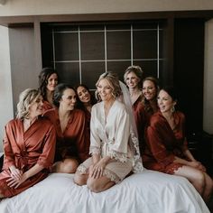 a group of women sitting on top of a bed in matching robes and smiling at the camera