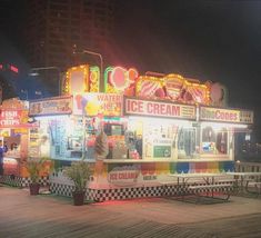 an ice cream stand is lit up at night with neon lights and checkered tables