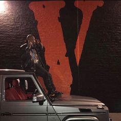 a man sitting on the hood of a truck talking on a cell phone in front of a giant shadow