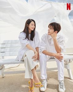 a man and woman sitting on a bench in front of a white sheeted wall