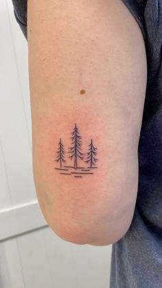 a person with a small tattoo on their arm that has three trees in the middle