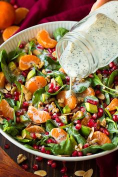 someone pouring dressing into a salad with oranges, spinach and pomegranate