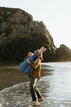 a man carrying a woman on his back while walking in the water at the beach