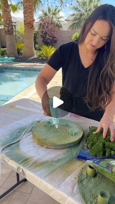 a woman cutting broccoli on top of a table next to a swimming pool