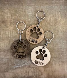 three wooden key chains with different designs on them, one has a dog's paw and the other has an animal's name