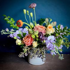 an arrangement of flowers in a white vase on a wooden table against a blue wall