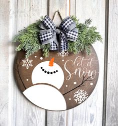 a snowman sign hanging on the side of a wooden door with evergreen and bow