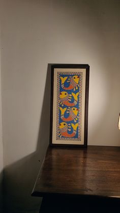 a table with a lamp on it next to a framed art piece and a painting