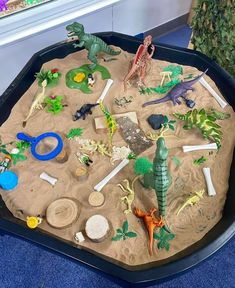 a sand tray filled with different types of toy animals and dinosaurs on top of it