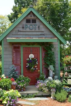 a small gray house with red door and green trim on the front, surrounded by potted plants