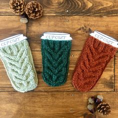 three knitted cup cozyies sitting on top of a wooden table next to pine cones