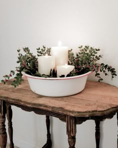 candles are lit in a bowl on a table with greenery and berries around it