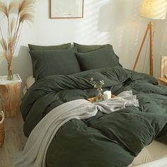 an unmade bed with green sheets and blankets on it in a white walled room